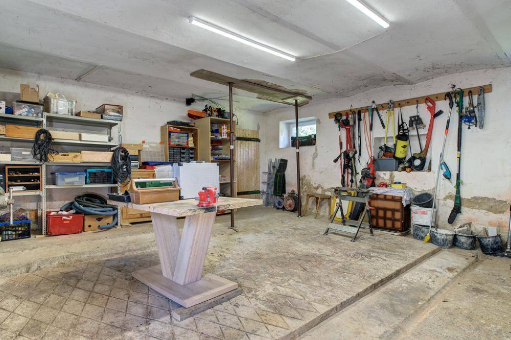 Geräumige Werkstatt mit Betonboden, Regalen und verschiedenen Werkzeugen an der Wand.