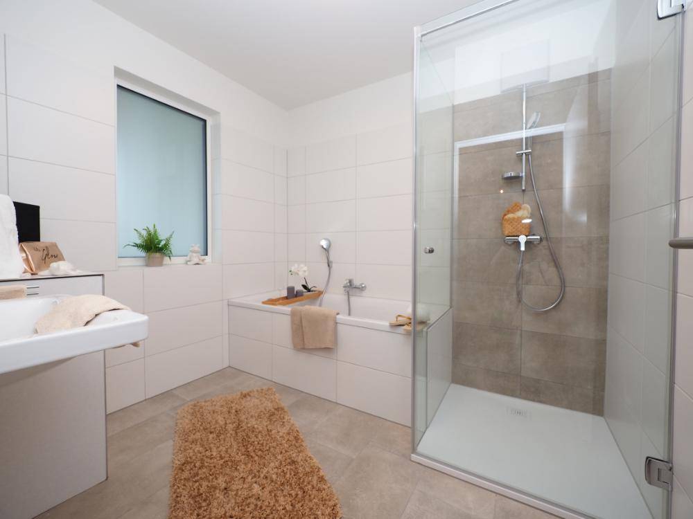 Modernes Badezimmer mit großer Dusche, Badewanne, Fenster und hellen Fliesen.