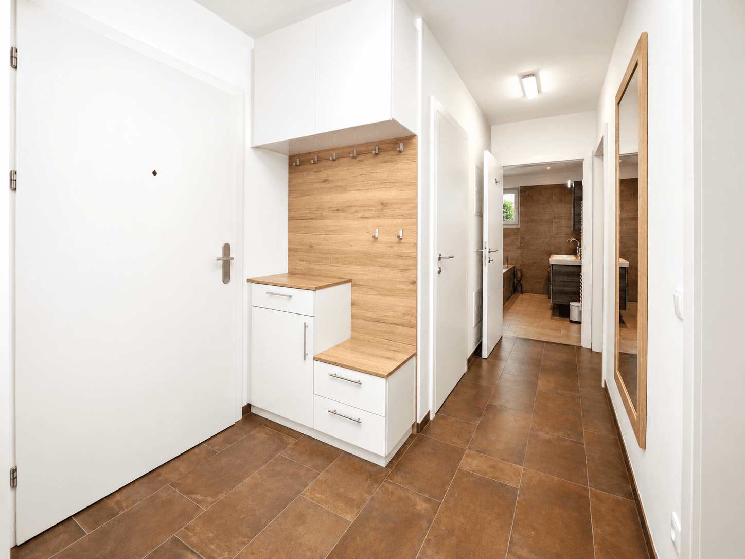Heller Eingangsbereich mit praktischen Einbauschränken, Garderobe und großem Spiegel.