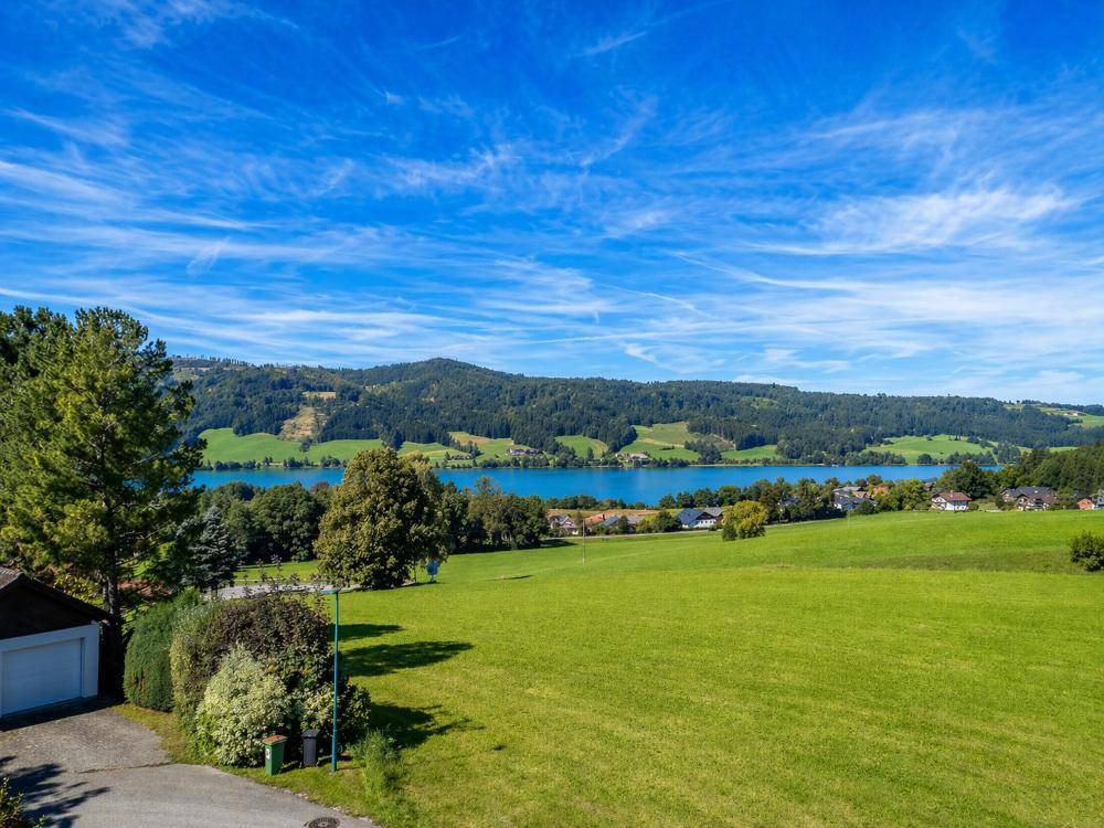 Panoramablick auf einen malerischen See, umgeben von sanften Hügeln und weiten grünen Feldern.