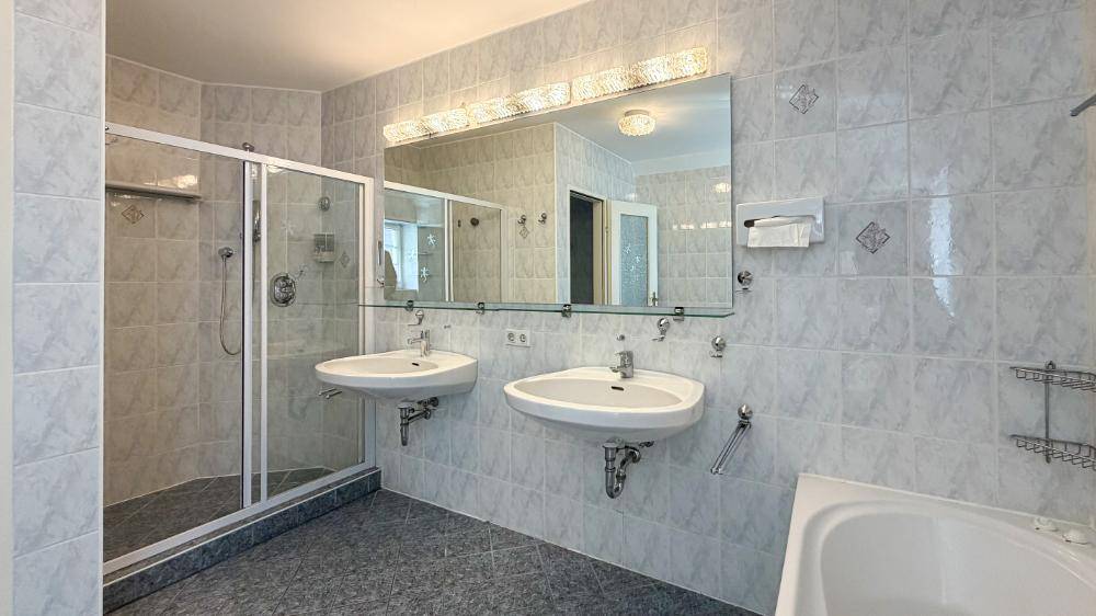 Helles Badezimmer mit Doppelwaschbecken, Duschkabine und Badewanne.