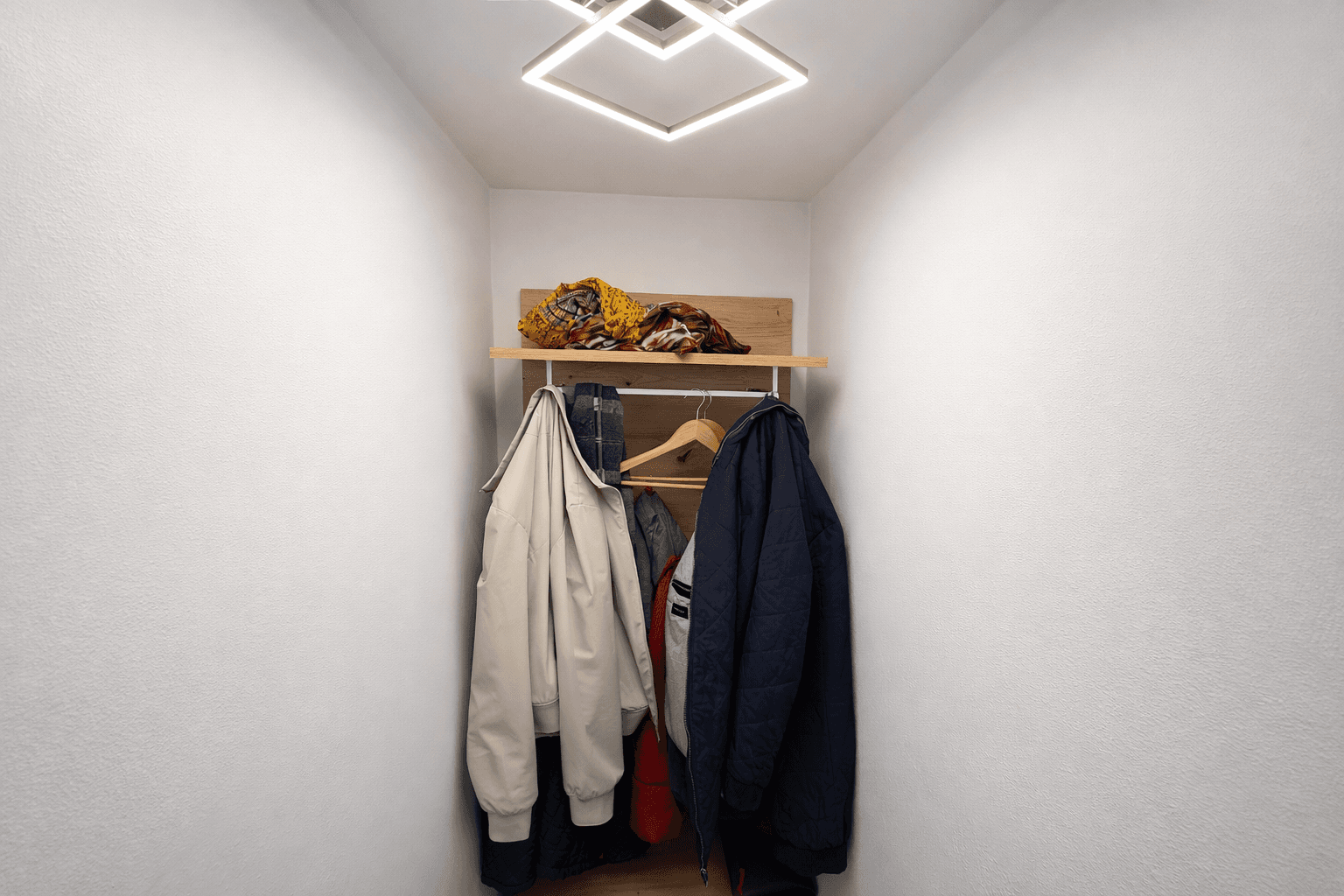 Kleiner Flurbereich mit Garderobe und moderner Deckenbeleuchtung für Jacken und Accessoires.