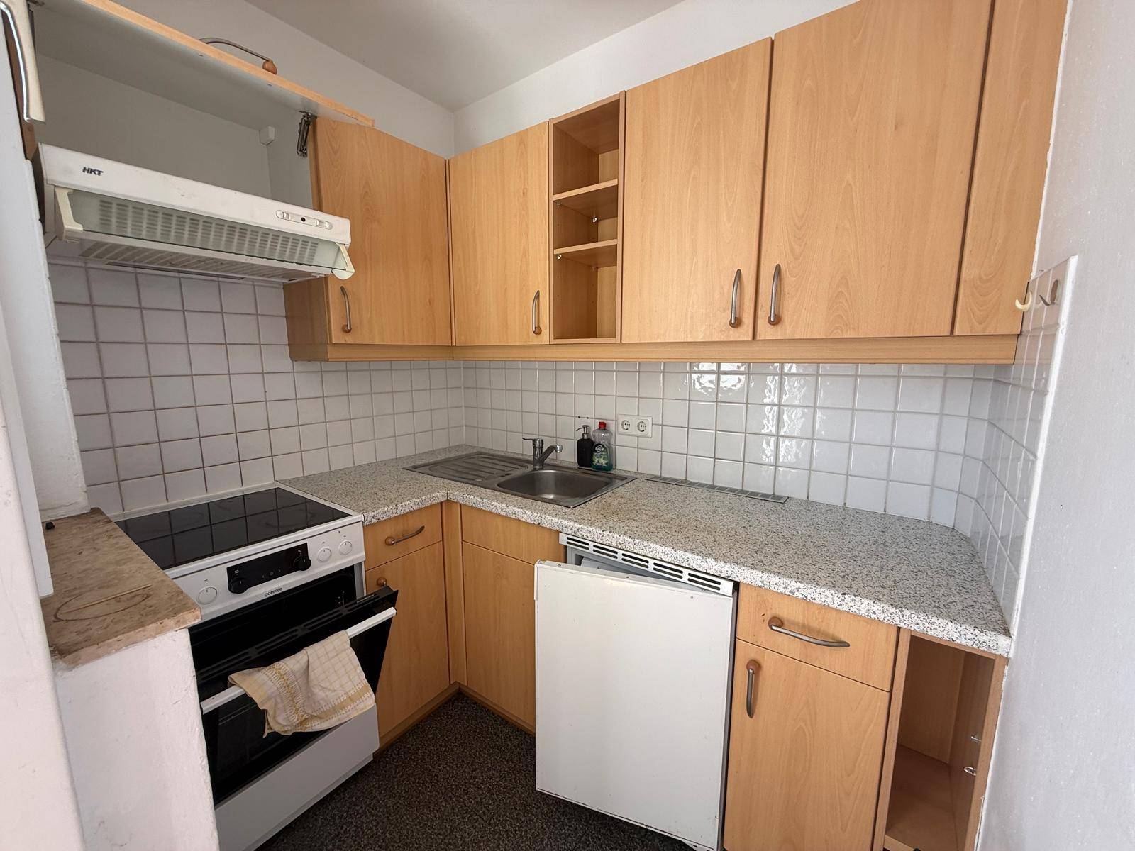 Funktionale Küche mit hellen Holzschränken, Fliesenrückwand und grundlegenden Geräten.
