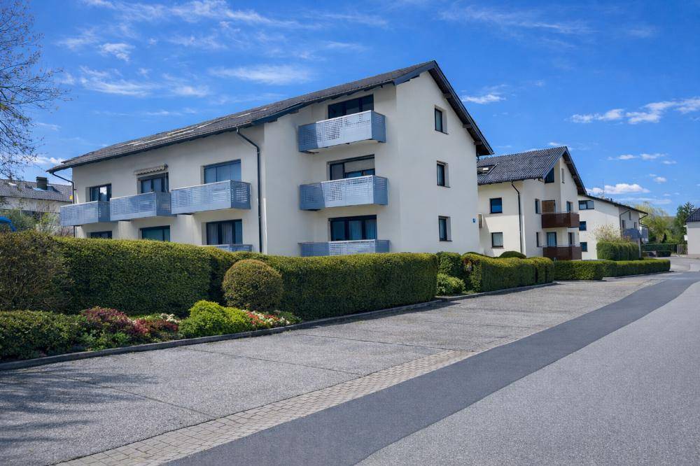Mehrfamilienhaus mit mehreren Balkonen und gepflegter Hecke, umgeben von Grünflächen.