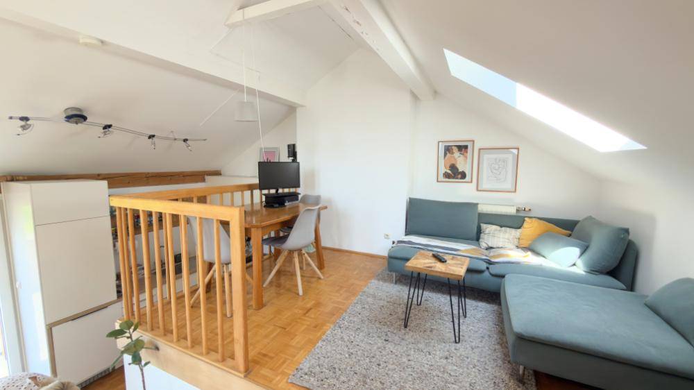 Heller Wohnbereich im Loft-Stil mit Dachschrägen, Holzboden und gemütlichem Sofa.