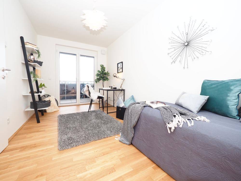 Helles Schlafzimmer mit Holzboden, Schreibtisch und Zugang zu einem französischen Balkon.