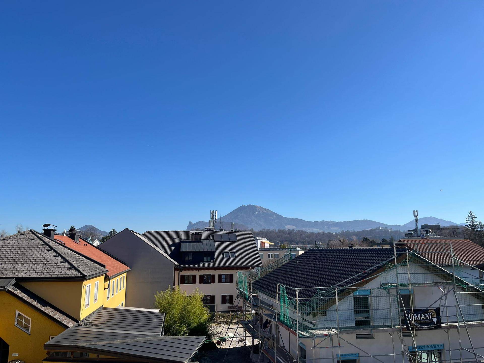 Panoramablick über die Dächer der Stadt mit Bergen im Hintergrund unter blauem Himmel.