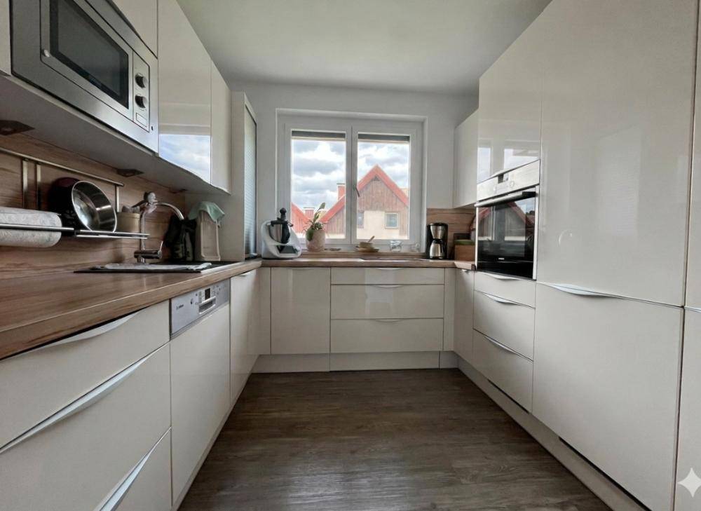 Helle Einbauküche mit weißen Schränken, Holzdetails und Blick aus dem Fenster.