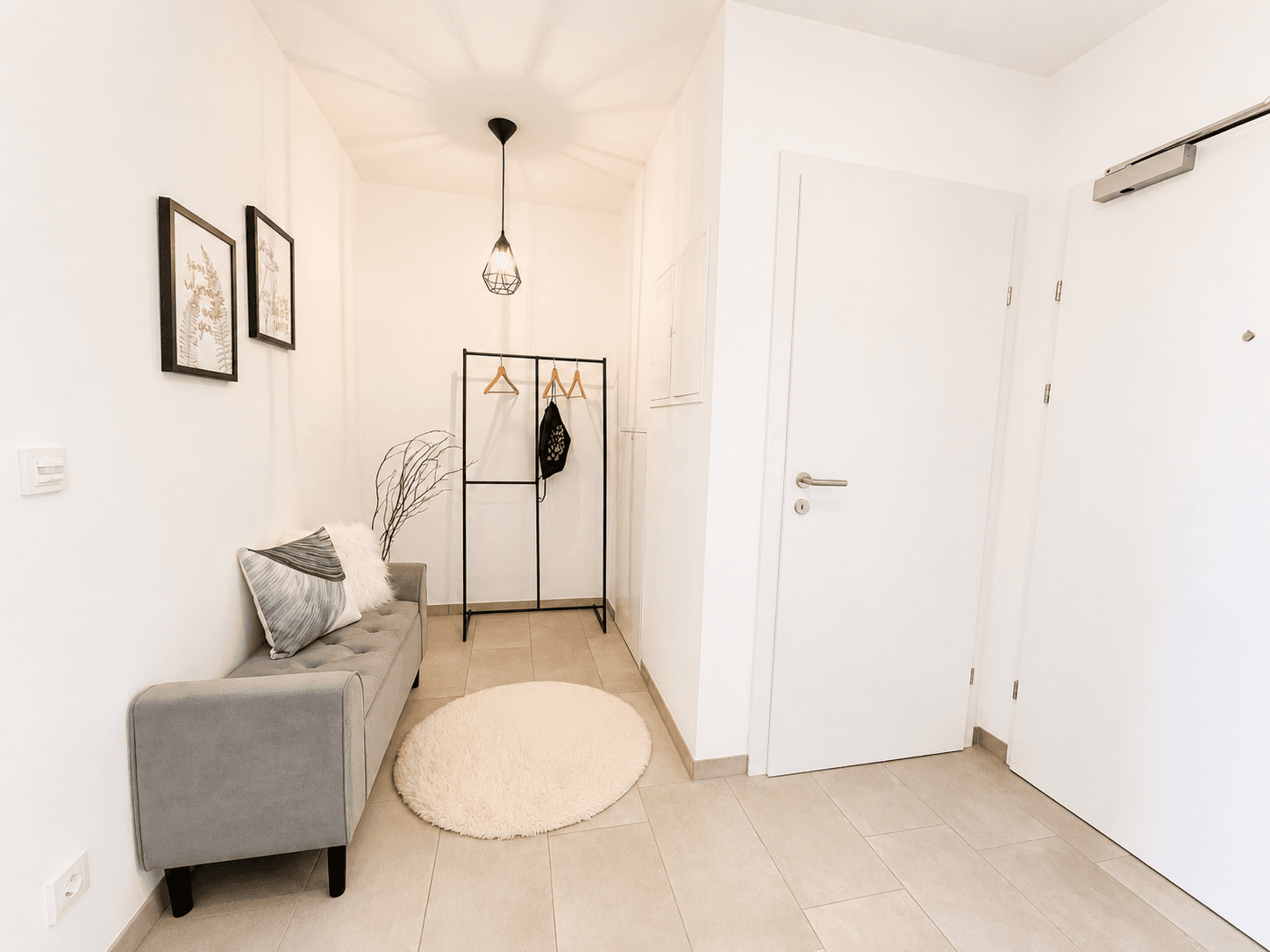 Heller Eingangsbereich mit Fliesenboden, Garderobe und kleiner Sitzbank.