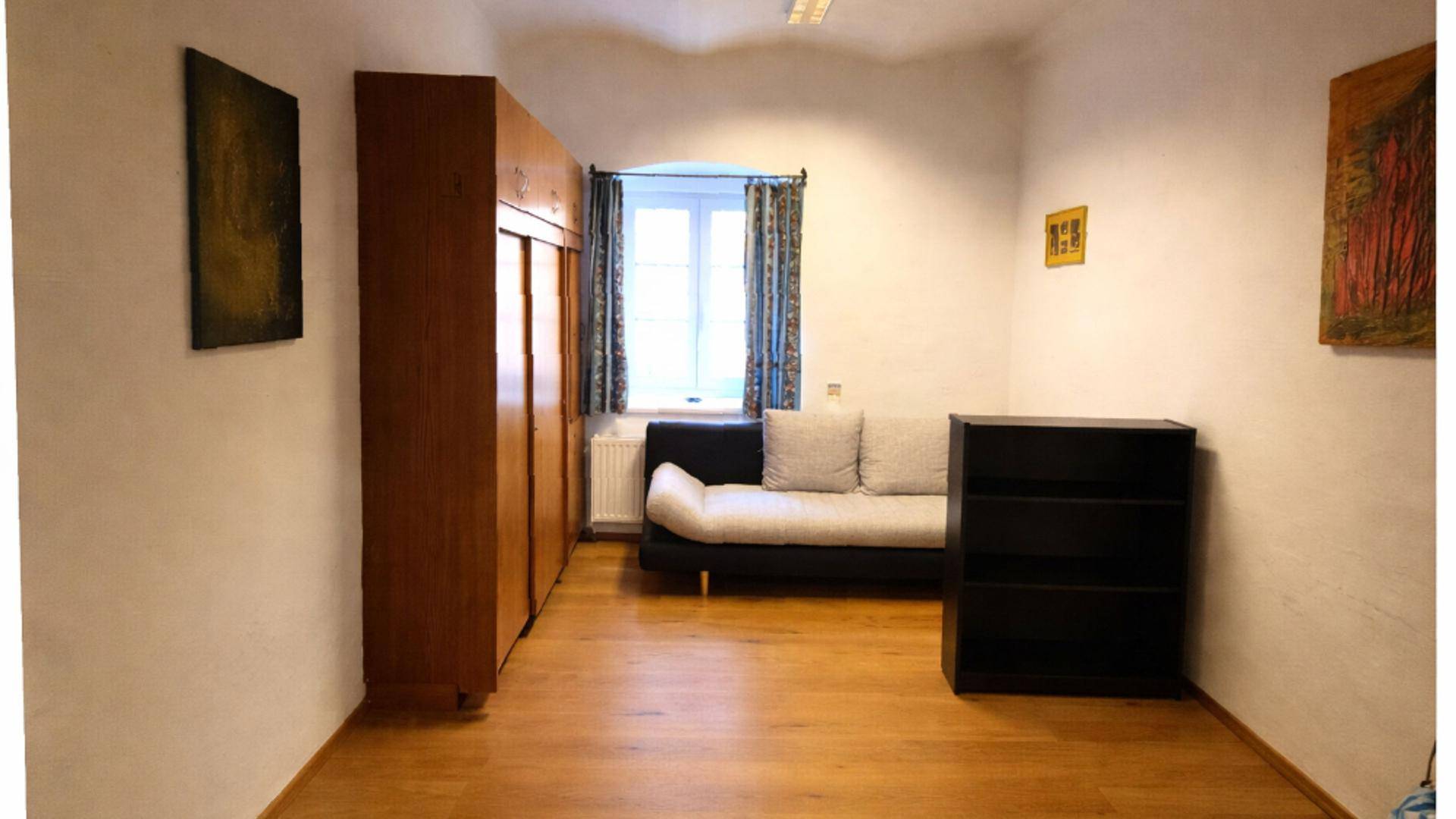 Schlafzimmer mit Holzboden, einem Kleiderschrank, einem Sofa und einem Fenster mit Vorhängen.