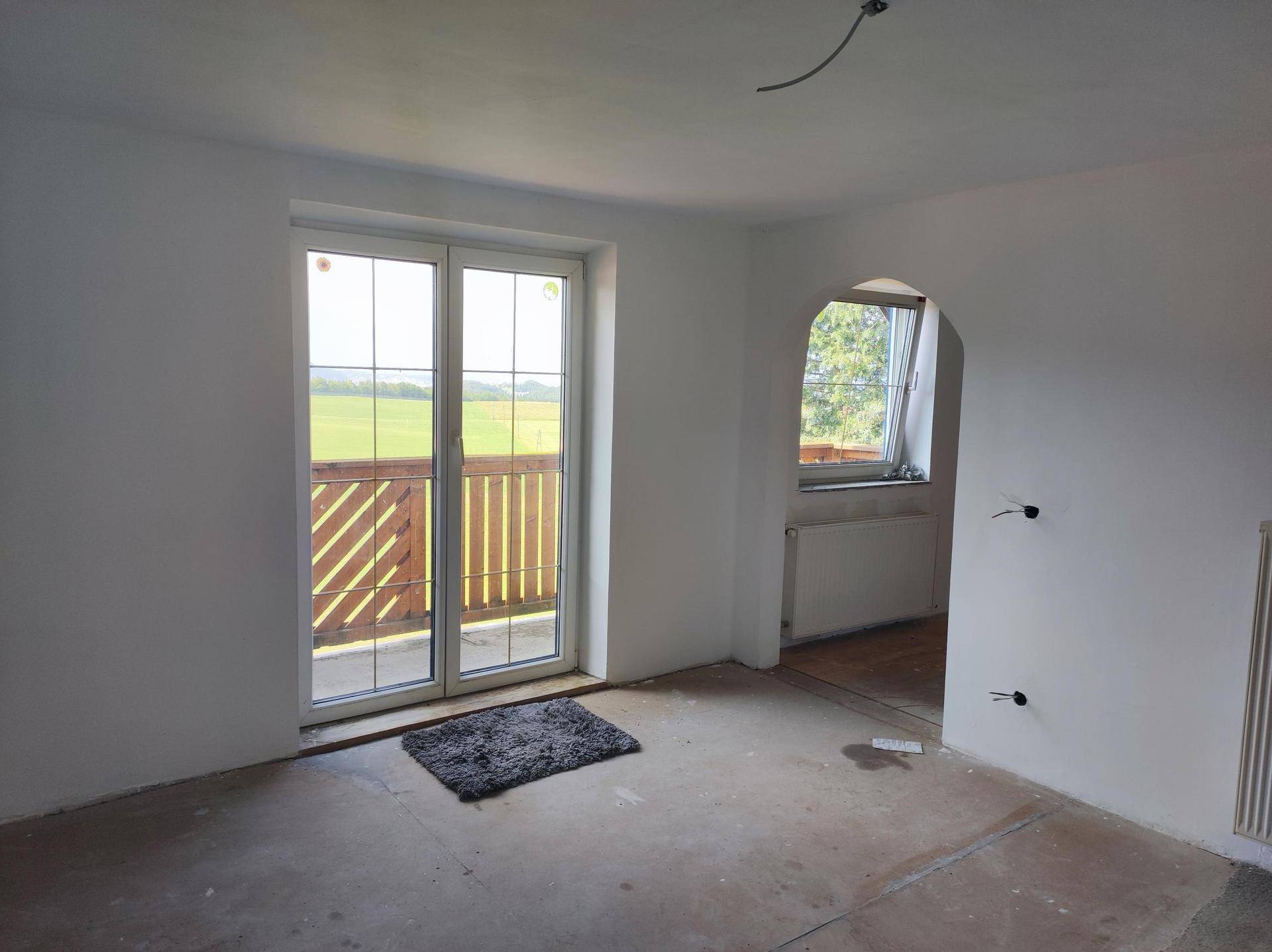 Heller Innenraum in Renovierung mit Zugang zu einem Balkon und einer Bogenöffnung zu einem weiteren Zimmer.
