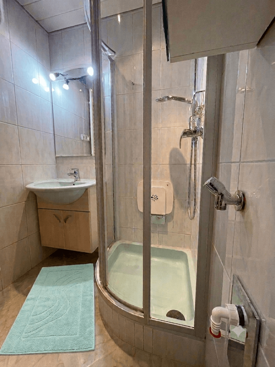 Kleines Badezimmer mit Eckduschkabine, Waschbecken mit Unterschrank und hellen Fliesen.