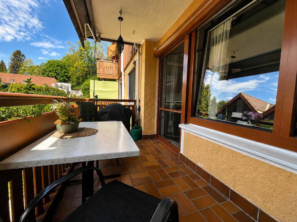 Sonniger Balkon mit Fliesenboden, Sitzgelegenheiten und Markise.