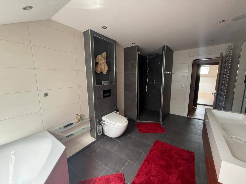 Modernes Badezimmer mit Dusche, Badewanne, Doppelwaschbecken und roten Akzenten.