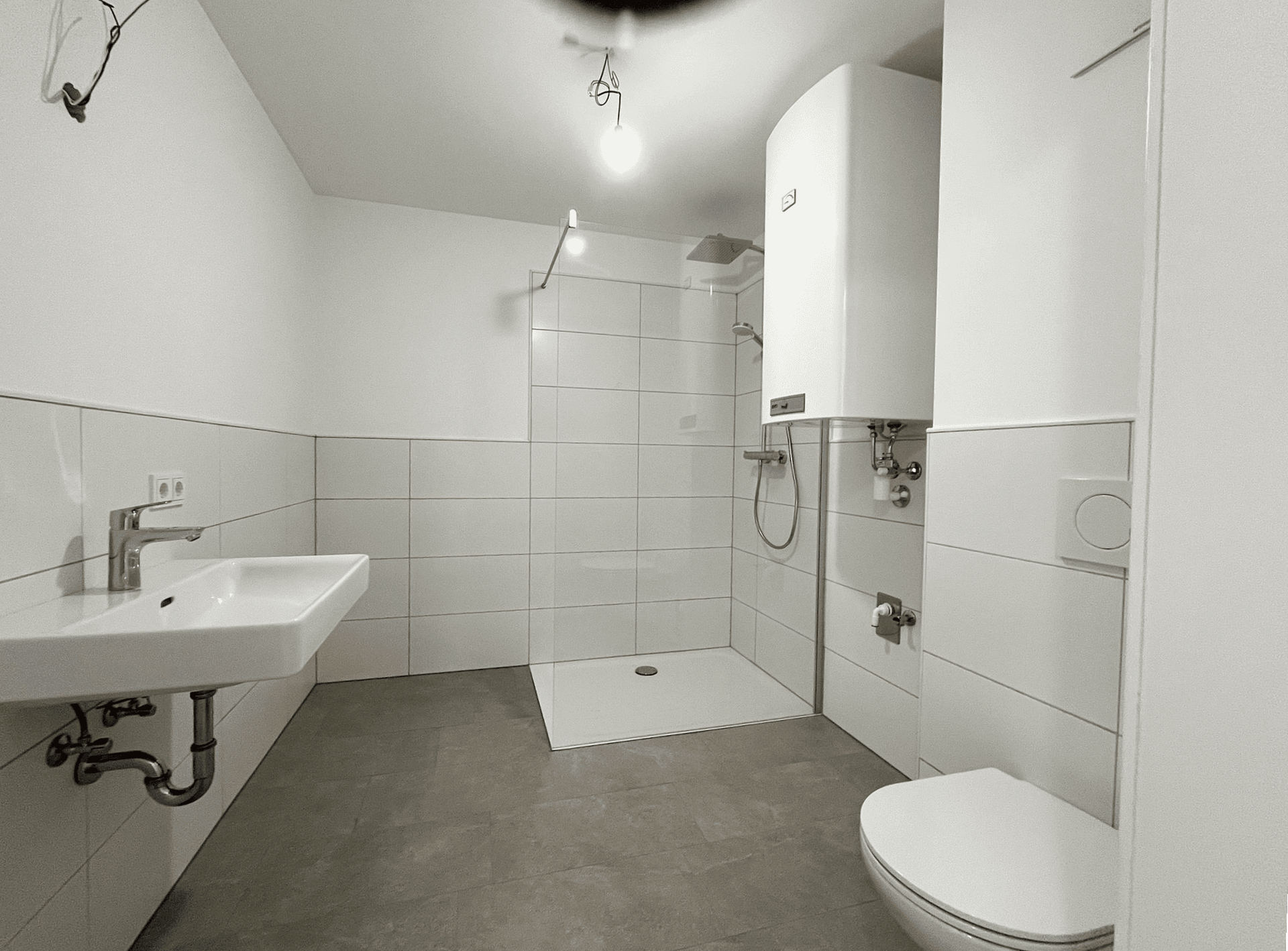 Modernes Badezimmer mit ebenerdiger Dusche, Wand-WC und Waschbecken in neutralen Farben.