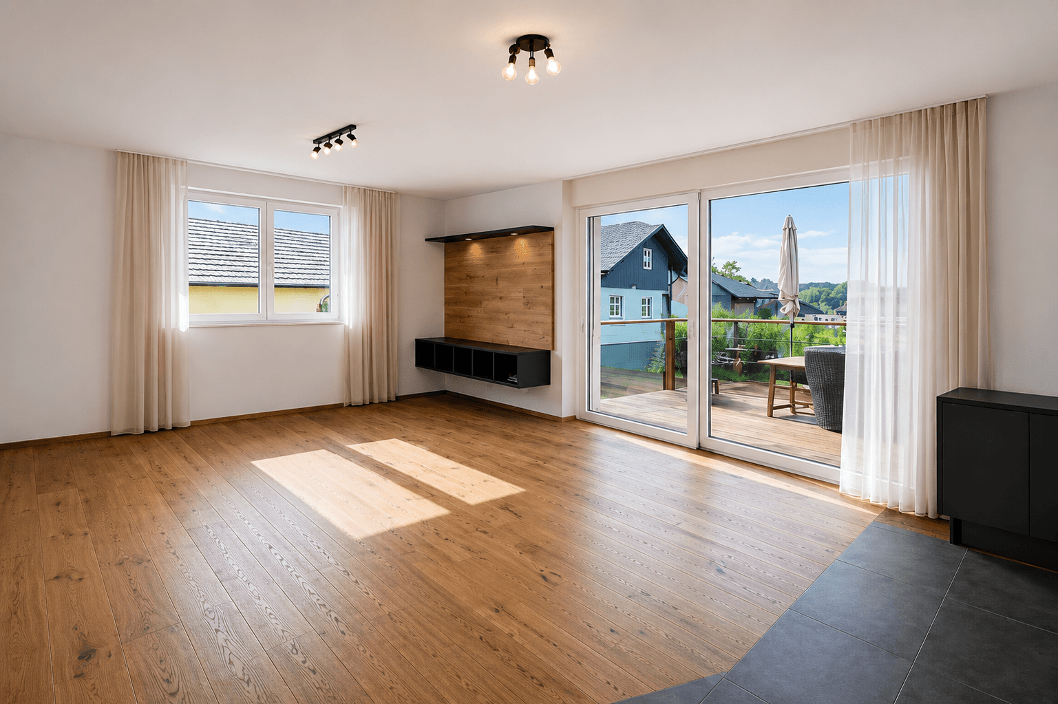 Helles Wohnzimmer mit Holzboden, großen Fenstern und Zugang zu einem Balkon oder einer Terrasse.