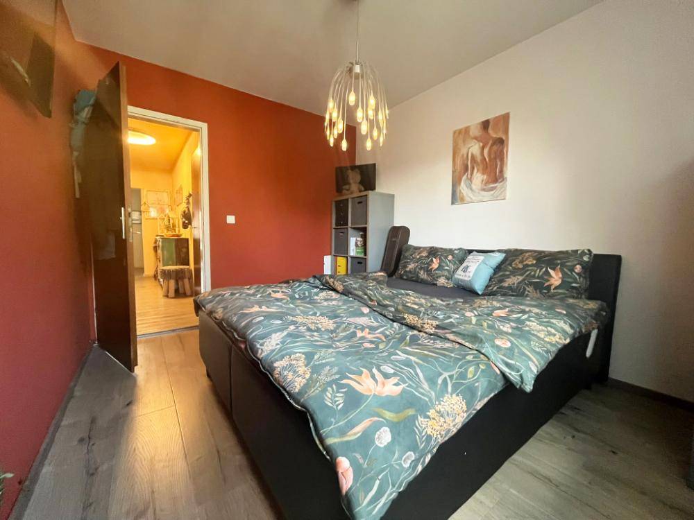 Schlafzimmer mit roter Wand, Holzboden und Zugang zu einem weiteren Raum.