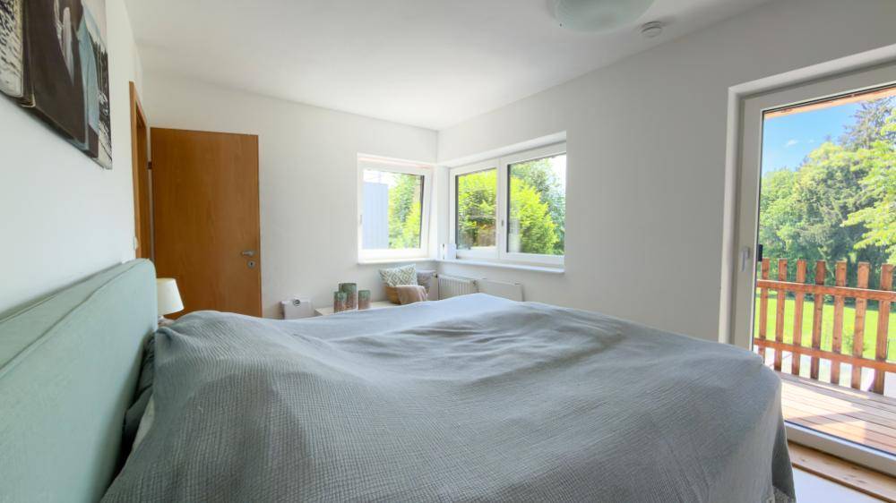 Schlafzimmer mit großem Fenster, Holzboden und direktem Zugang zu einem Außenbereich.