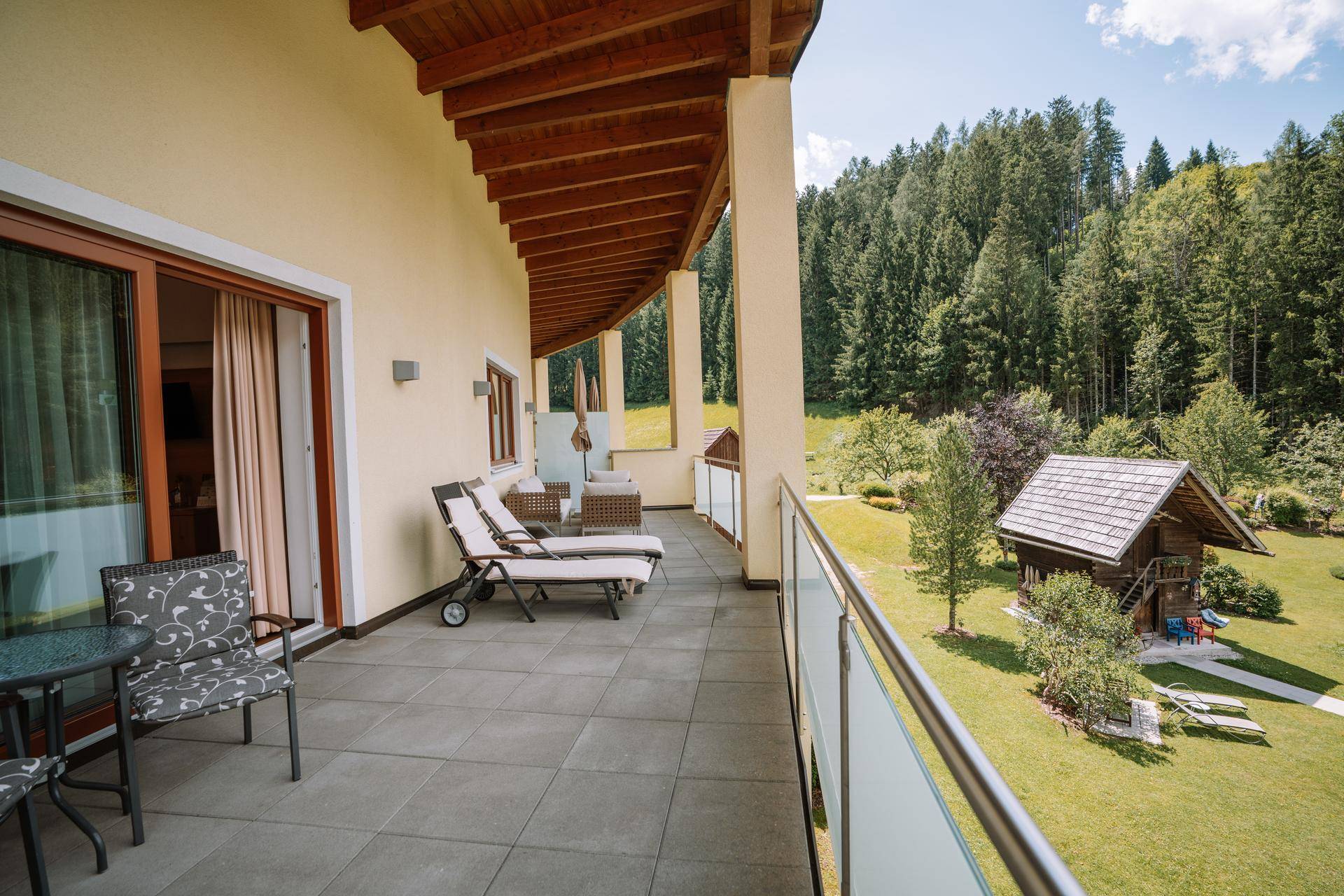 Breiter Balkon mit Sitzgelegenheiten und Blick auf die grüne Landschaft und ein kleines Holzhaus.