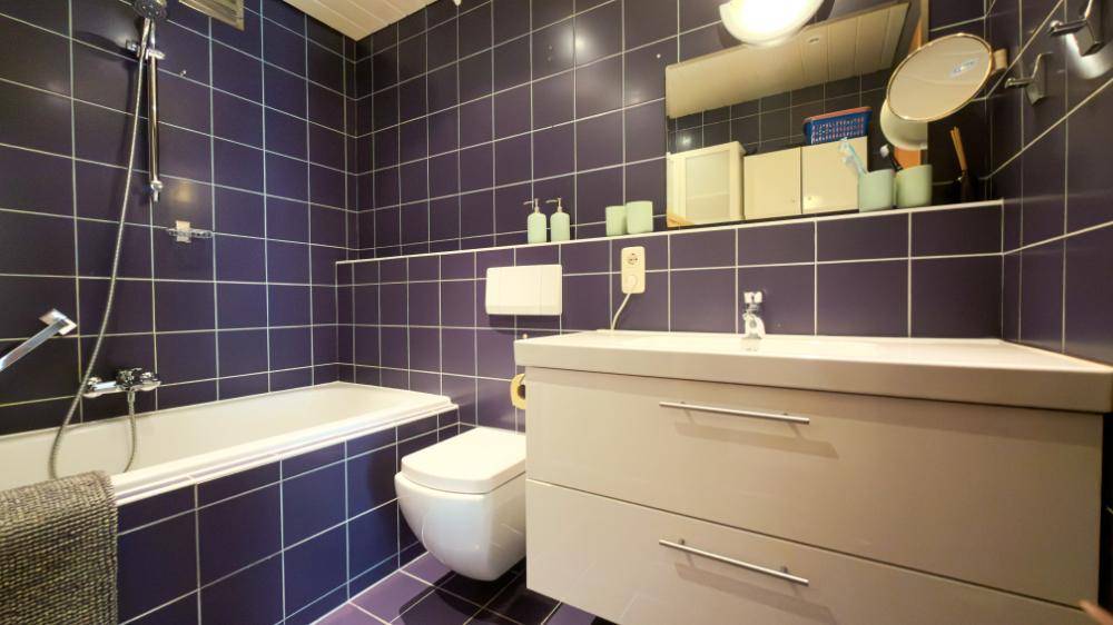 Badezimmer mit blauen Fliesen, Badewanne, WC und Waschtisch mit Unterschrank.