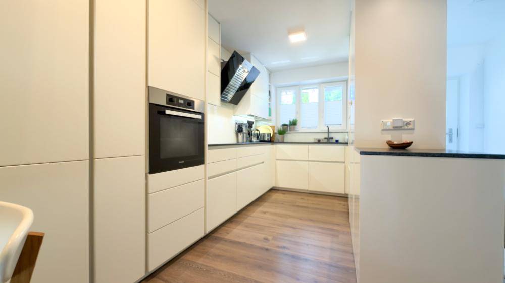 Moderne Einbauküche mit weißen Schränken, integrierten Geräten und Holzboden.