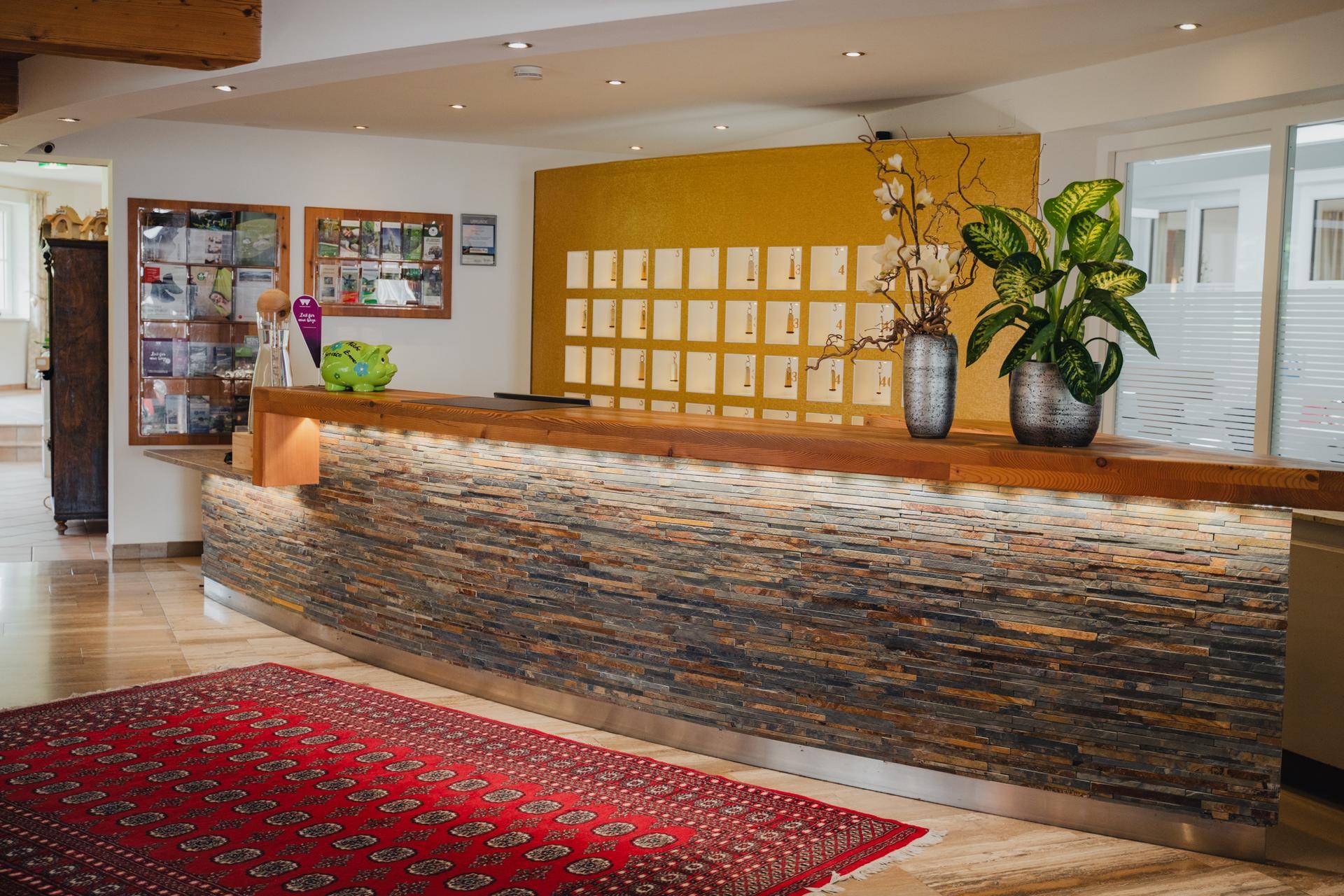 Moderne Hotelrezeption mit Natursteinverkleidung, Holztheke und dekorativen Pflanzen.