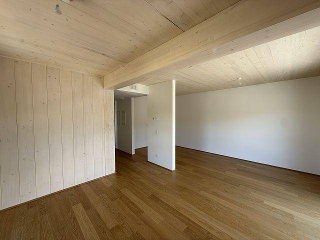 Geräumiger, unmöblierter Raum mit Holzboden und Holzdecke, ideal für offenes Wohnen.