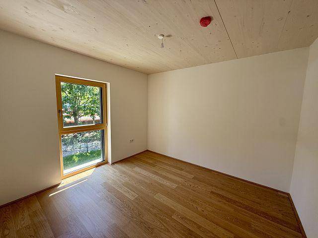 Helles Schlafzimmer mit Holzboden und großem Fenster, bietet einen angenehmen Blick ins Grüne.