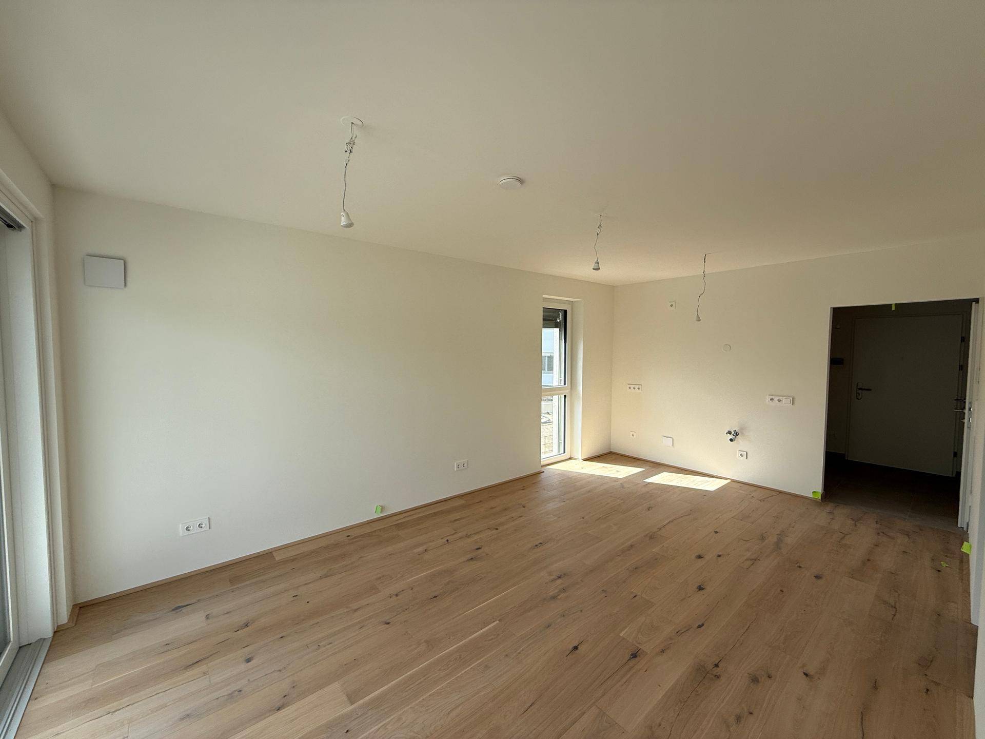 Lichtdurchfluteter Raum mit Holzboden und einem Fenster, das Tageslicht hereinlässt.