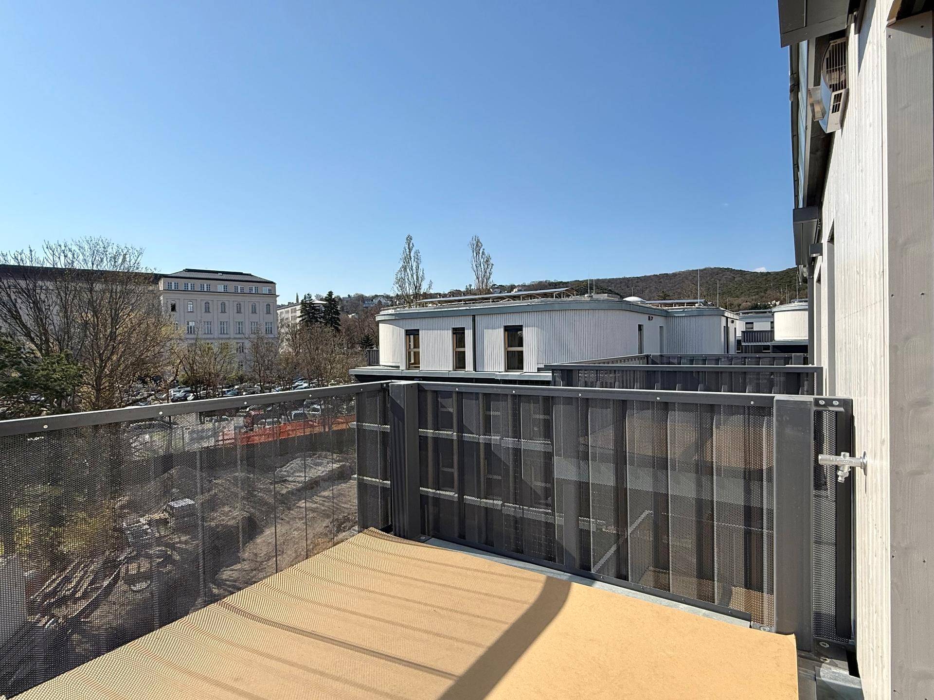 Geräumiger Balkon mit Metallgeländer und Blick auf die umliegenden Gebäude und Grünflächen.