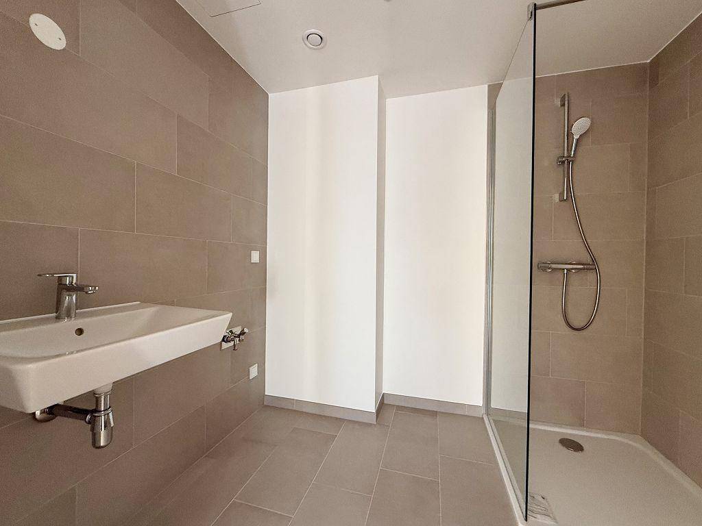 Modernes Badezimmer mit beigefarbenen Fliesen, Einzelwaschbecken und einer Duschkabine.