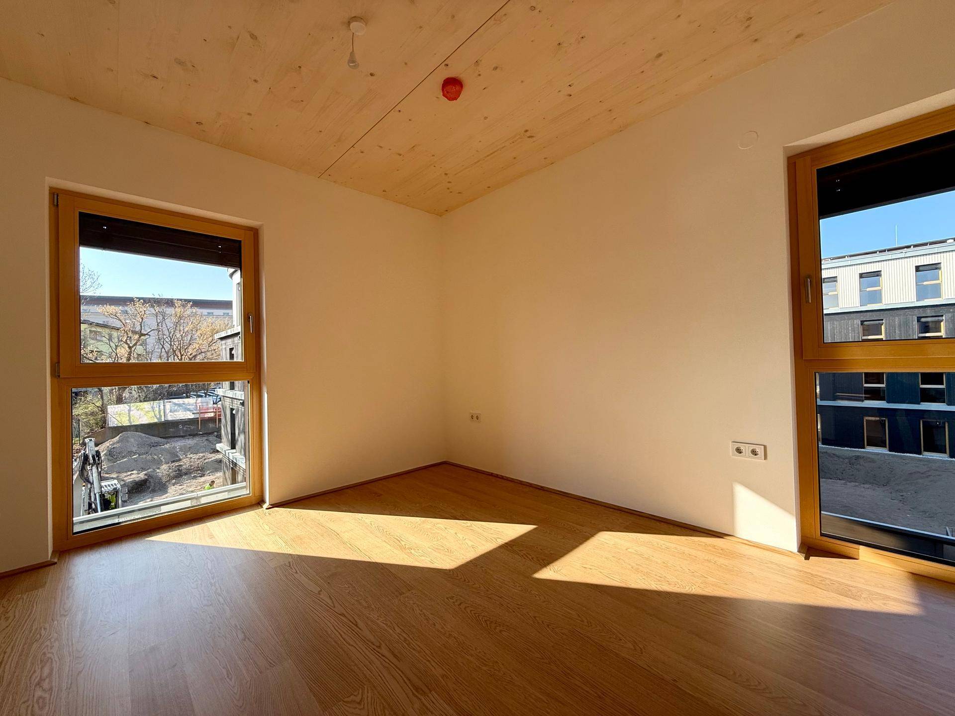 Helles Schlafzimmer mit Holzboden und zwei großen Fenstern, die viel Tageslicht hereinlassen.
