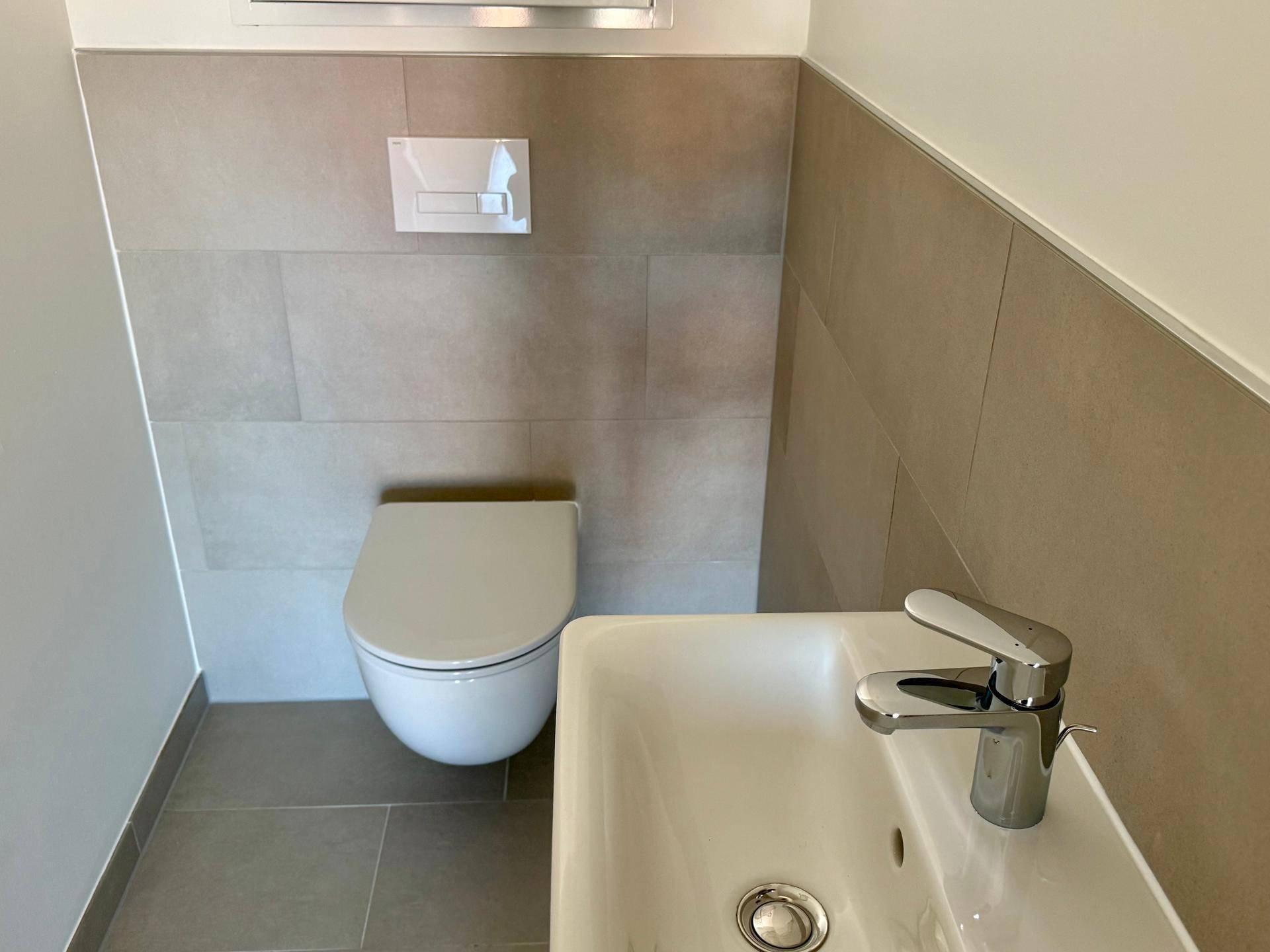 Kleines Gäste-WC mit modernem Wand-WC und kompaktem Waschbecken in neutralen Farbtönen.