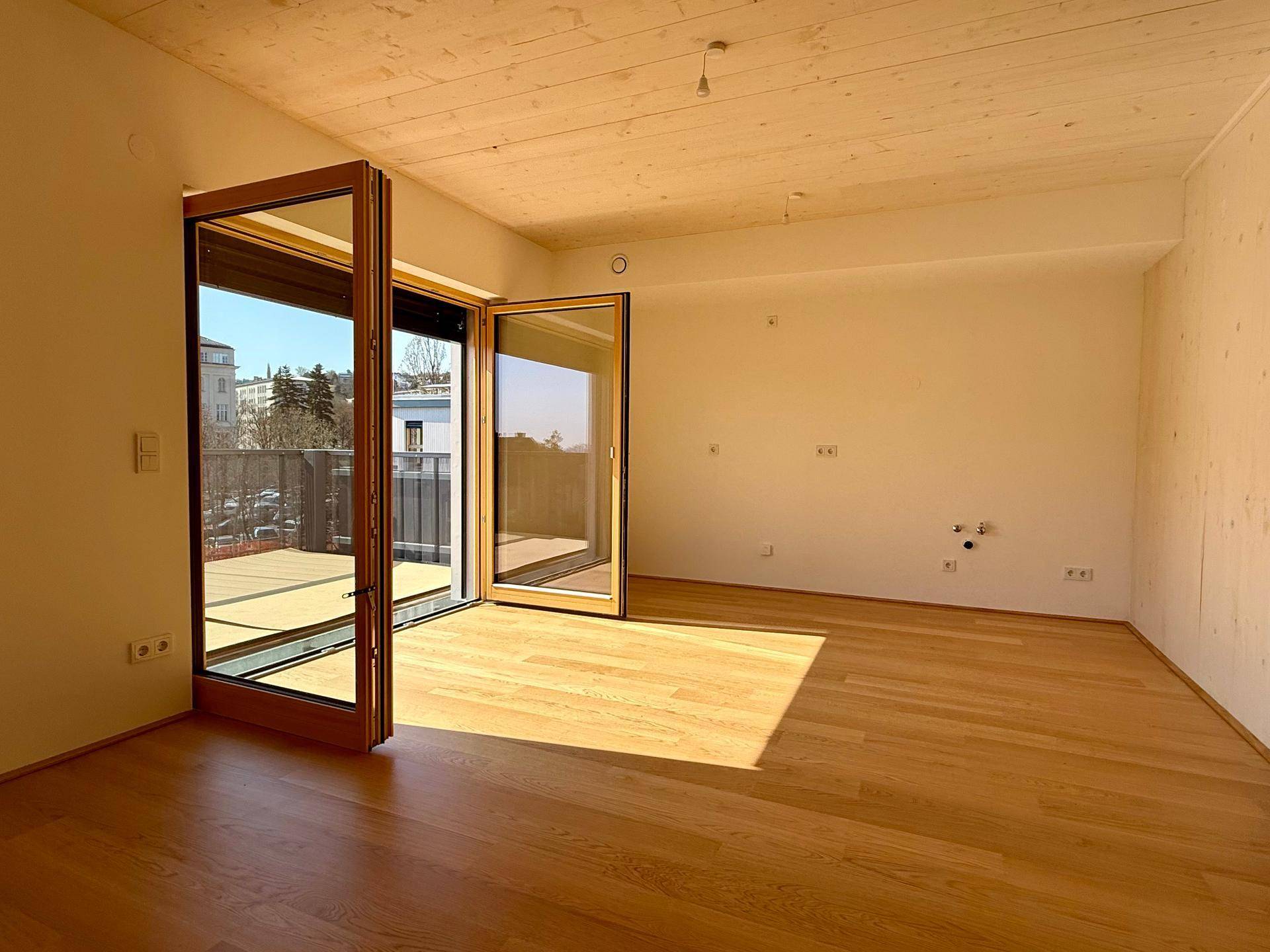 Geräumiges, helles Zimmer mit Holzboden und breitem Zugang zum Außenbereich.