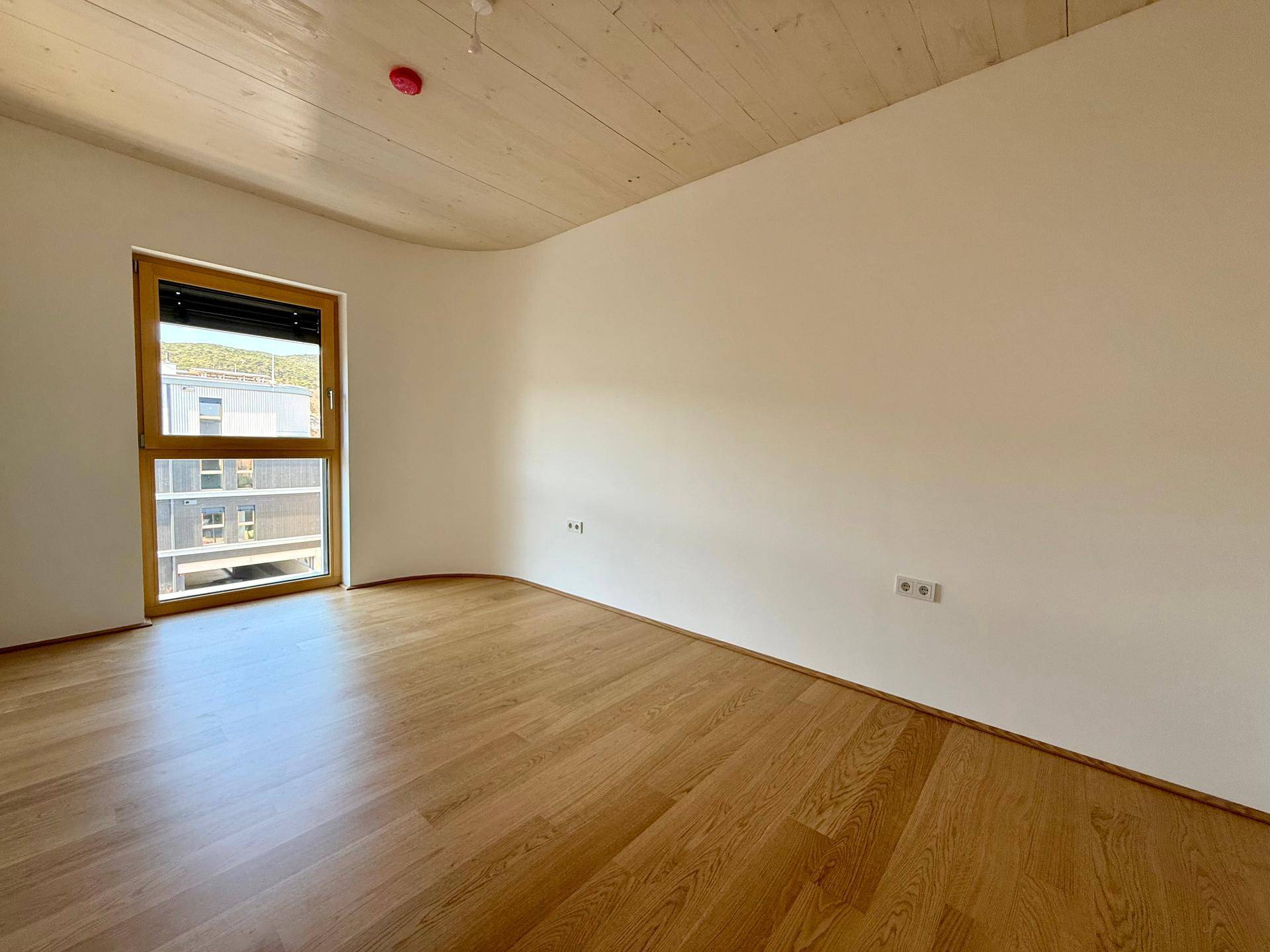 Ruhiges Zimmer mit Holzboden und einem Fenster, das den Raum mit natürlichem Licht füllt.