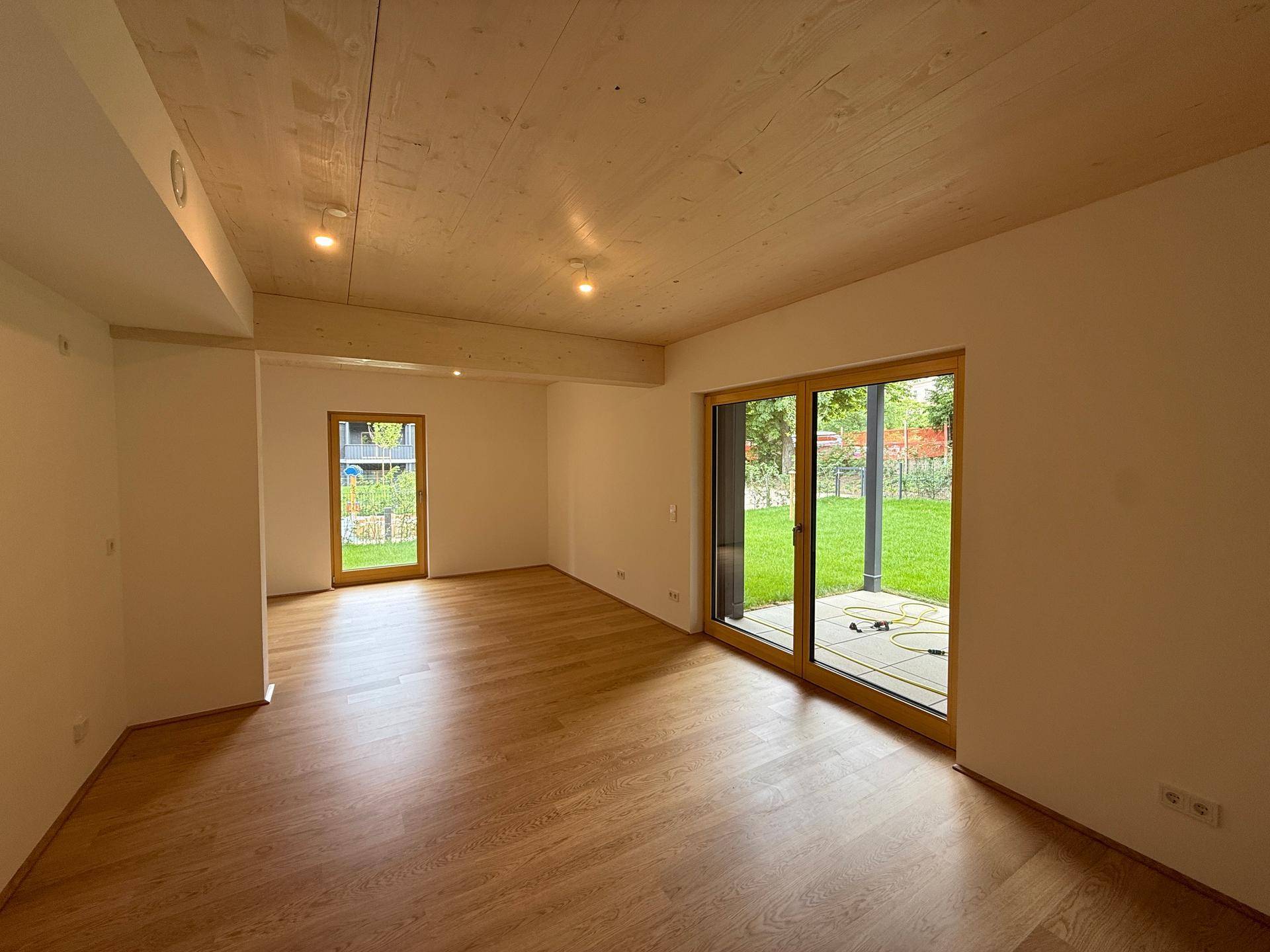 Geräumiger Wohnbereich mit Holzboden, Holzdecke und großer Schiebetür zur Terrasse und zum Garten.
