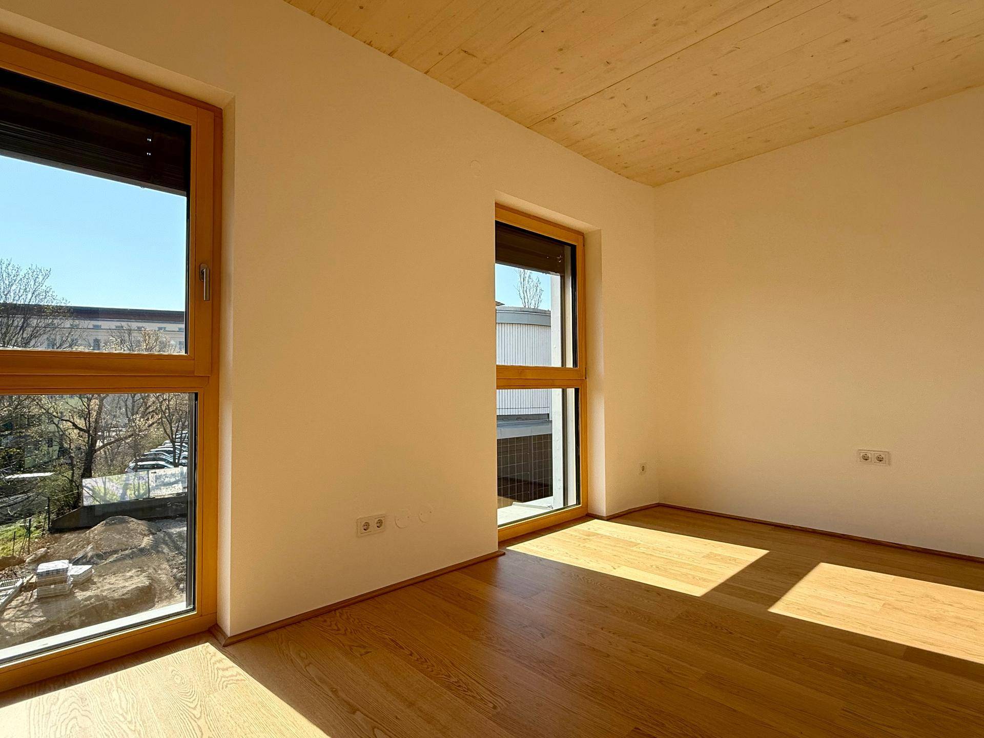 Helles Zimmer mit Holzboden und großen Fenstern, die eine angenehme Atmosphäre schaffen.