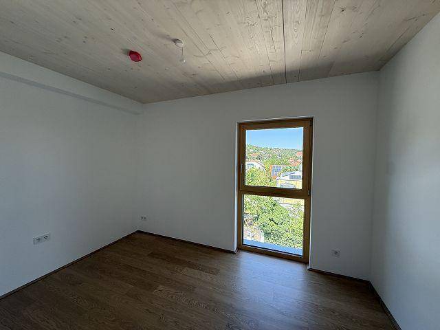 Helles Schlafzimmer mit Holzboden, Holzdecke und einem großen Fenster mit Ausblick.