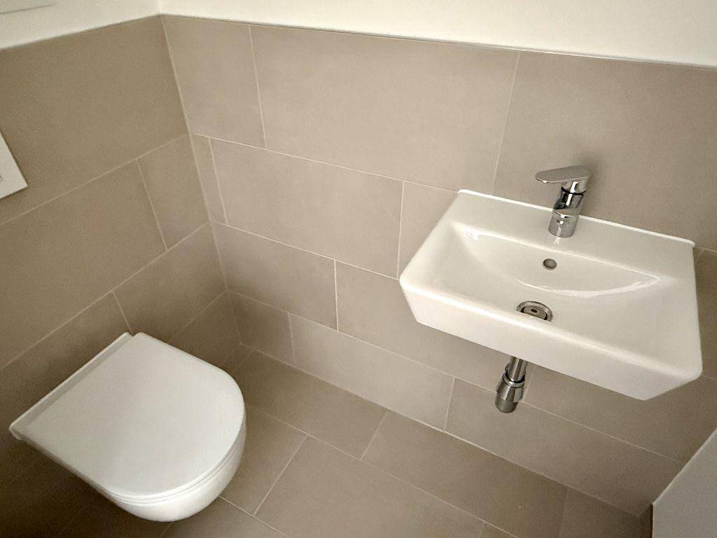 Modernes Gäste-WC mit Wand-WC und kleinem Waschbecken, ausgestattet mit hellen Fliesen.
