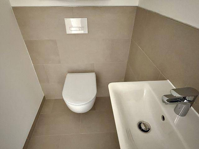 Gäste-WC mit wandhängender Toilette, kleinem Waschbecken und modernen Fliesen.