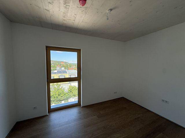 Sonniges Schlafzimmer mit Holzboden, Holzdecke und einem Fenster, das viel Tageslicht hereinlässt.