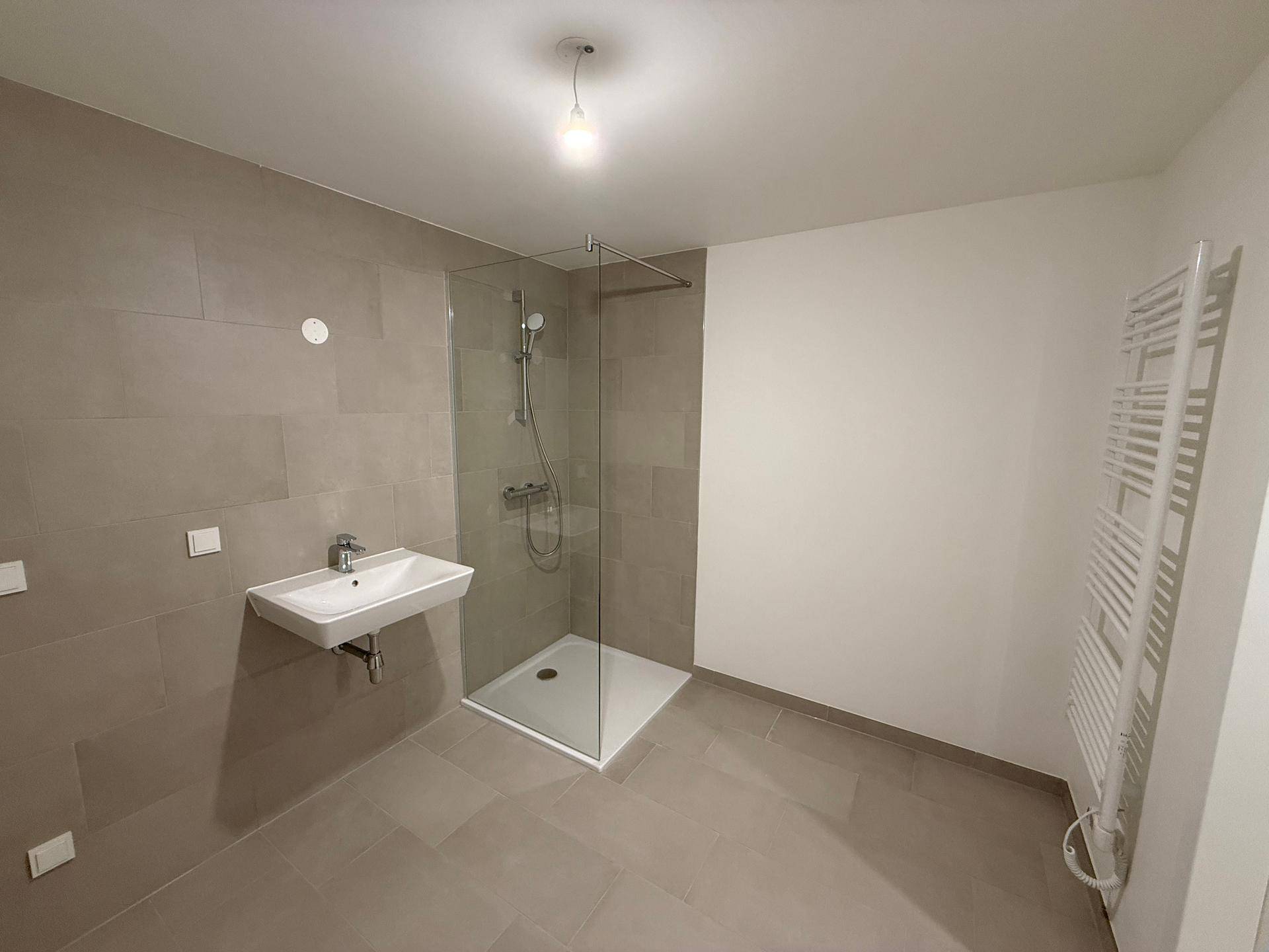 Modernes Badezimmer mit grauen Fliesen, ebenerdiger Dusche und beheiztem Handtuchhalter.