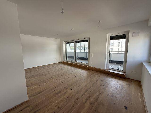 Lichtdurchfluteter Wohnraum mit Parkettboden und zwei Zugängen zu den Außenbereichen des Apartments.