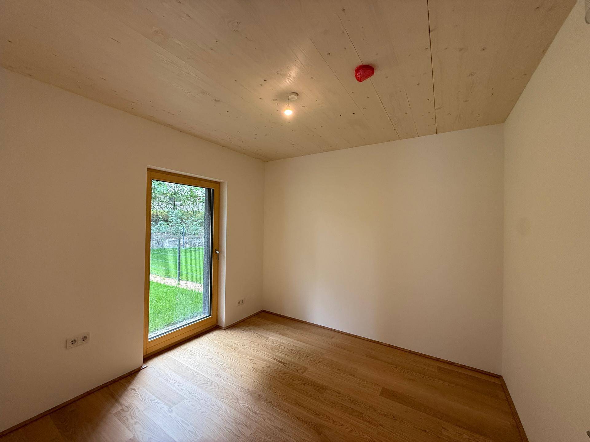 Helles Schlafzimmer mit Holzboden, Holzdecke und direktem Zugang zum privaten Gartenbereich.