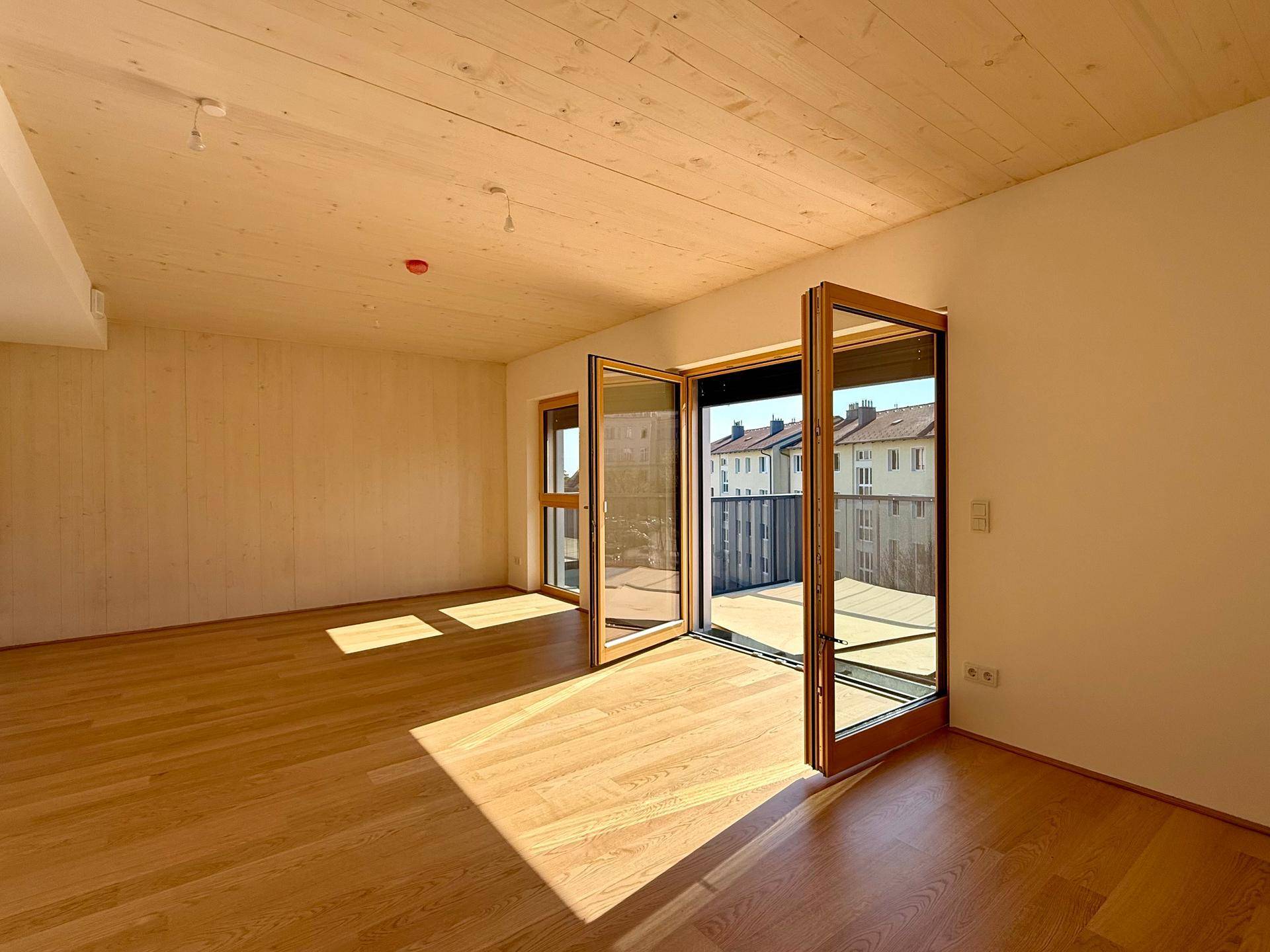 Lichtdurchfluteter Wohnraum mit Holzboden und Zugang zu einem Balkon, ideal für offenes Wohnen.