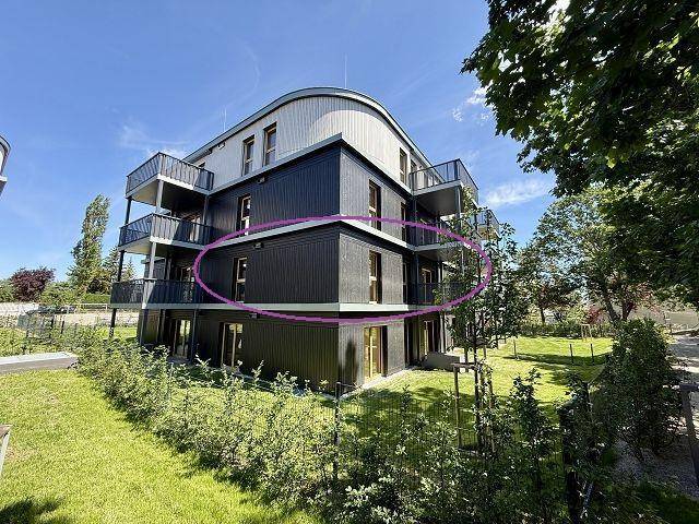 Moderne Wohnanlage mit dunkler Fassade und Balkonen, umgeben von viel Grün und Bäumen.