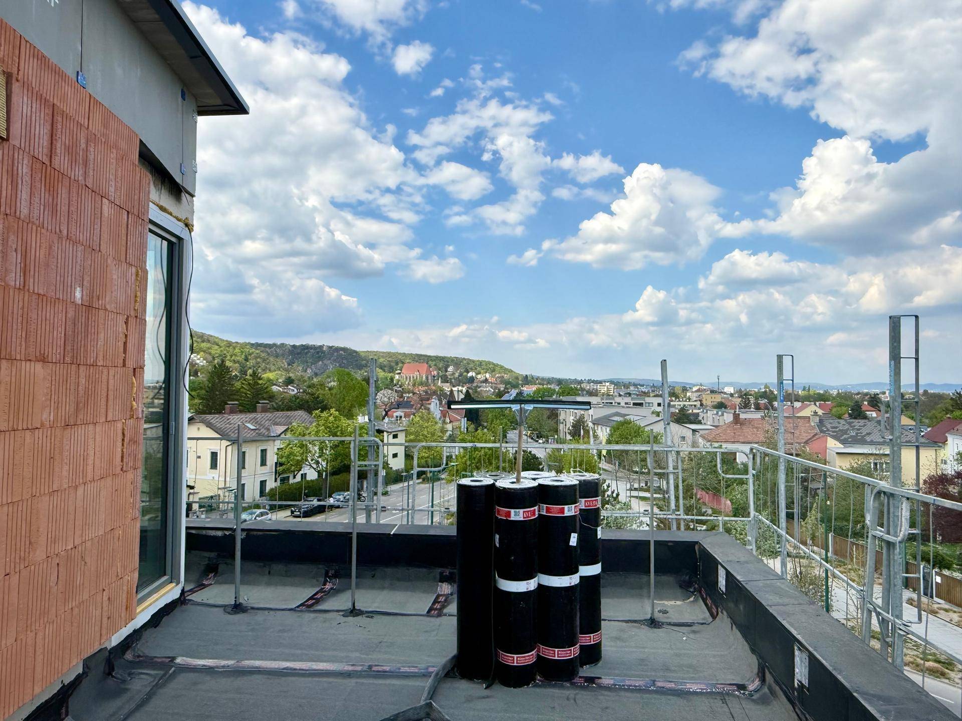 Dachterrasse im Bau mit Baumaterialien und Panoramablick über die Stadt und die Landschaft.