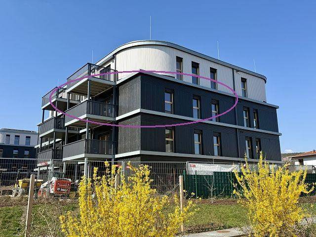 Modernes Mehrfamilienhaus mit dunkler Fassade und Balkonen, umgeben von Baustelle.