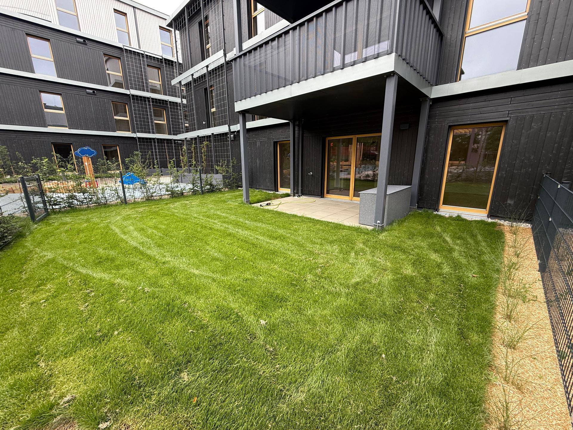 Grüner Gartenbereich mit Terrasse und Blick auf den Spielplatz, umgeben von moderner Architektur.