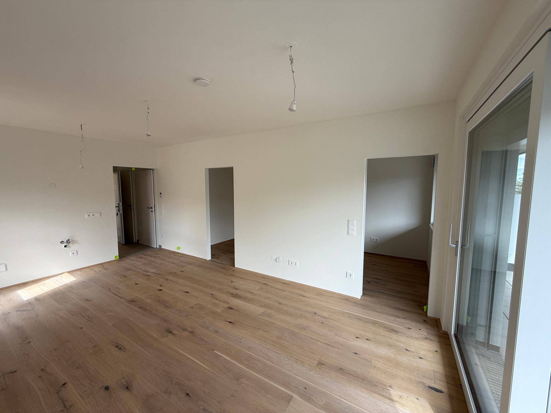 Geräumiges, unmöbliertes Zimmer mit hellem Holzfußboden und mehreren Türöffnungen.